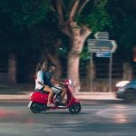 A couple rides a red scooter at night in Rodos, Greece, capturing a lively street scene.